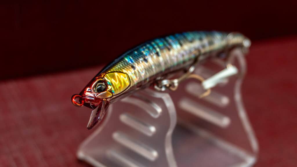 Lure Tide Minnow Sprat in primo piano, esposto su un supporto trasparente, con riflessi colorati e dettagli realisitici.
